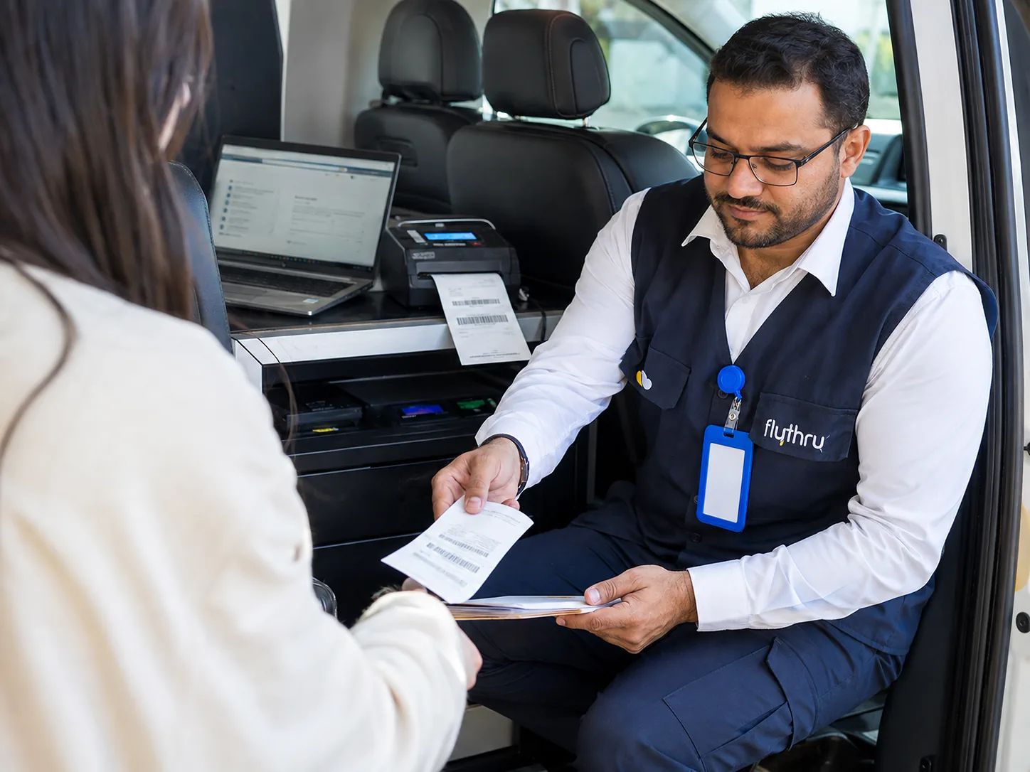 A FlyThru agent hands over freshly printed travel documents at the in-van check-in station